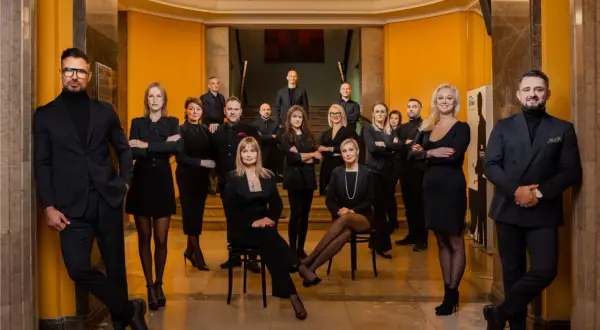 Grupa profesjonalistów w eleganckich czarnych strojach pozuje w holu.