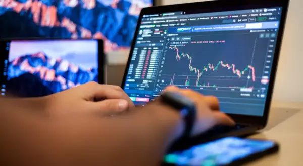 Osoba analizuje wykresy na laptopie, ucząc się, day trading co to jest. Obok leży smartfon.