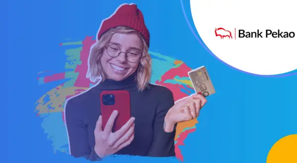 Uśmiechnięta młoda kobieta w czerwonej czapce trzyma telefon i kartę bankową Pekao.