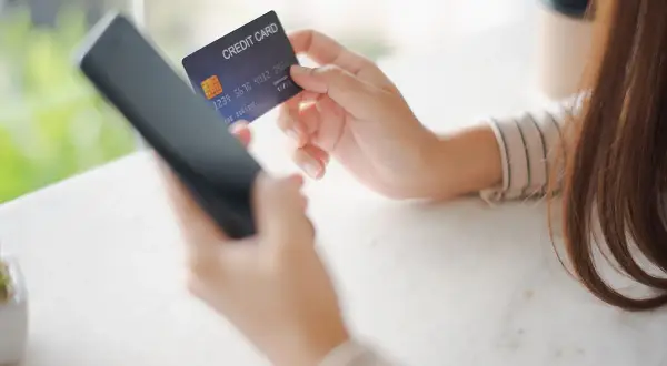 Kobieta trzyma kartę kredytową i telefon, przygotowując się do płatności online. W razie problemów z transakcją, może skorzystać z procedury chargeback.