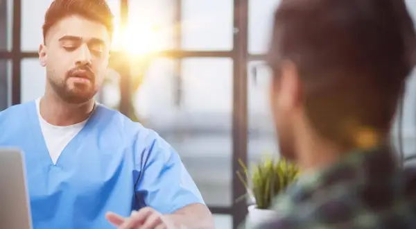 Lekarz w niebieskim kitlu rozmawia z pacjentem. Czy do psychiatry potrzebne jest skierowanie? Zapytaj lekarza.