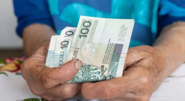 Dłonie starszej osoby trzymają banknoty 100 zł. Czy to wystarczy na najniższą emeryturę 2026?