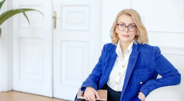 Kobieta w okularach i niebieskiej marynarce trzyma notatnik. Planujesz otwarcie firmy w 2025? Sprawdź dostępne dotacje!