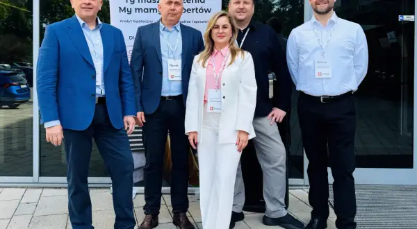 Pięć osób w eleganckich strojach stoi przed budynkiem, za nimi baner z logo "m Finanse".