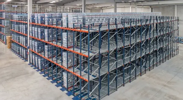 Duże regały magazynowe z towarami ułożonymi zgodnie z zasadą fifo. Towary na rolkach, gotowe do wysyłki.