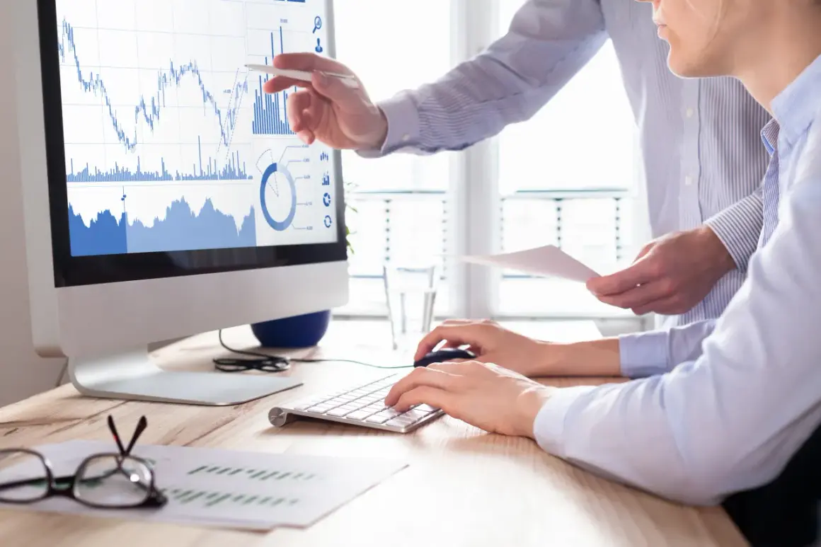 Dwóch analityków analizuje wykresy giełdowe na monitorze, dyskutując o strategii buy limit co to.
