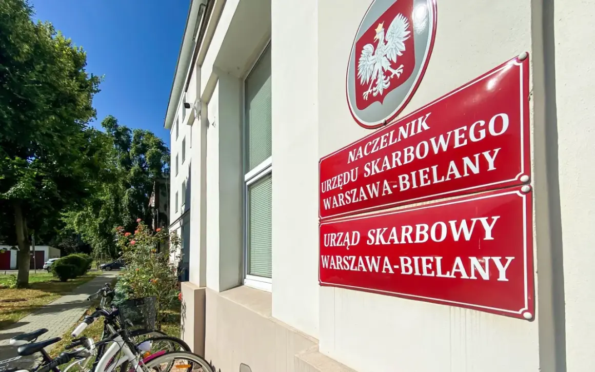 Tablice Urzędu Skarbowego Warszawa-Bielany. Obok stoją rowery, a w tle drzewa i błękitne niebo. sd-z2.