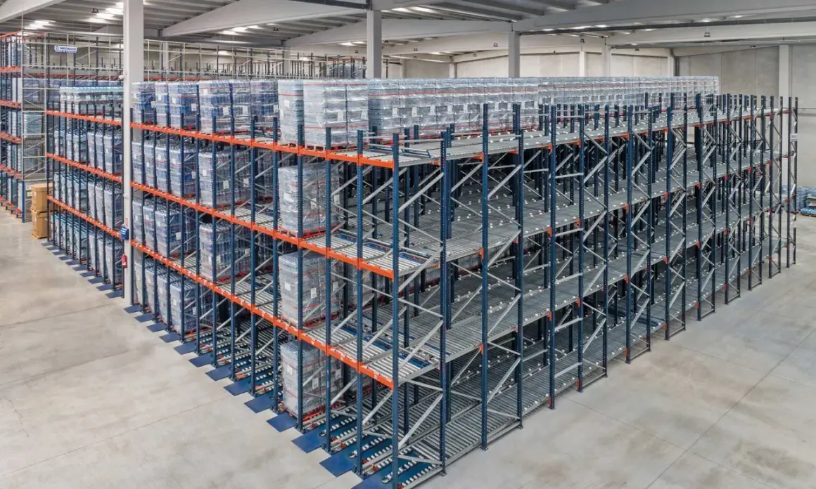 Duże regały magazynowe z towarami ułożonymi zgodnie z zasadą fifo. Towary na rolkach, gotowe do wysyłki.