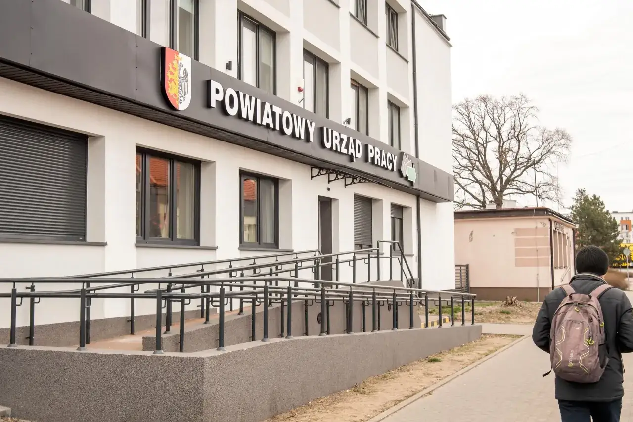 Mężczyzna z plecakiem idzie chodnikiem obok Powiatowego Urzędu Pracy. Budynek ma napis