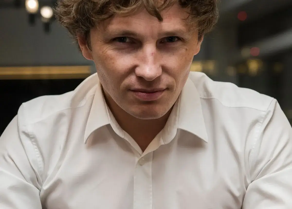 Zbliżenie na twarz Rafała Zaorskiego w białej koszuli. Jego spojrzenie jest intensywne, a włosy lekko potargane.