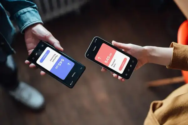 Dwie osoby dokonują płatności przez telefon. Jedna pokazuje "Payment Received $45.00", druga "Payment Sent $45.00". Czy Revolut jest bezpieczny? Tak, transakcje są szyfrowane.