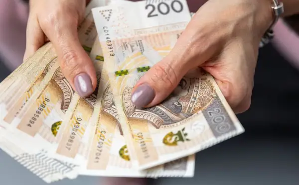 Dłonie trzymające stos banknotów 200 zł. Czy emerytura kapitałowa jest korzystna? Pieniądze to klucz do przyszłości.