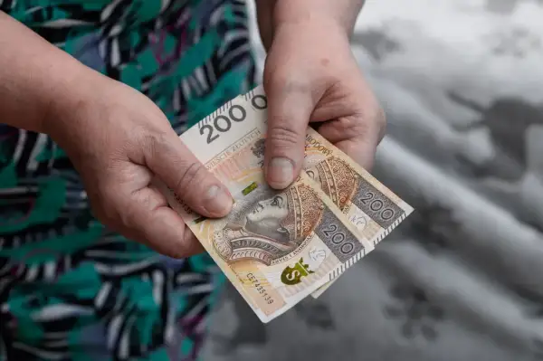 Dwie stuzłotowe banknoty w dłoniach. Czy to już wiadomo, ile wynosi zasiłek pielęgnacyjny?