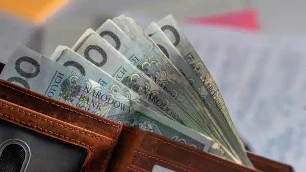 Portfel z polskimi banknotami 100 zł. W tle dokumenty, być może związane ze świadczeniem pielęgnacyjnym 2026.