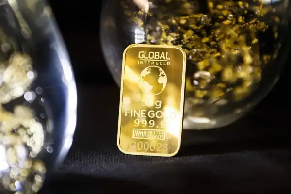 Sztabka 50g czystego złota 999.9, błyszcząca na tle szkła z płatkami złota.