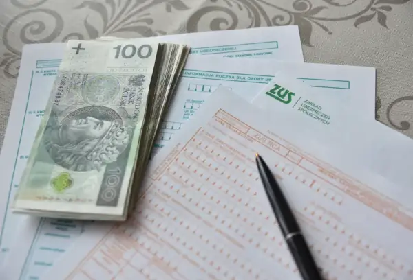 Stos papierów z ZUS, pieniądze i długopis sugerują, jak obliczana jest emerytura.