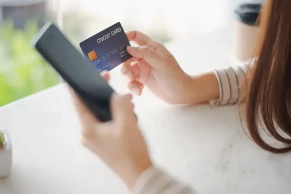 Kobieta trzyma kartę kredytową i telefon, przygotowując się do płatności online. W razie problemów z transakcją, może skorzystać z procedury chargeback.