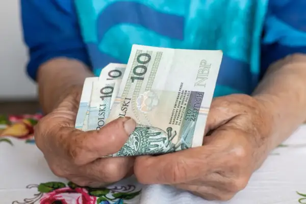 Dłonie starszej osoby trzymają banknoty 100 zł. Czy to wystarczy na najniższą emeryturę 2026?