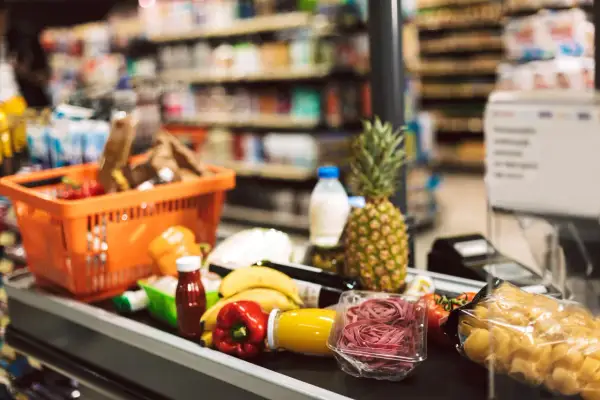 Koszyk z zakupami na taśmie w supermarkecie. Owoce, warzywa, makaron i napoje – typowe produkty FMCG, czyli szybko zbywalne towary.