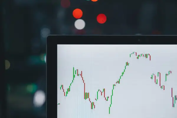 Wykres świecowy na ekranie laptopa pokazuje zmienny kurs USD JPY. W tle rozmyte światła miasta.