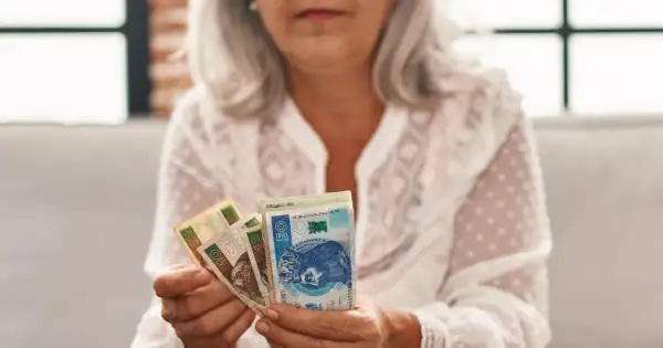 Kobieta z siwymi włosami trzyma polskie banknoty. To symbol oszczędności na emeryturę kapitałową dla kobiet.