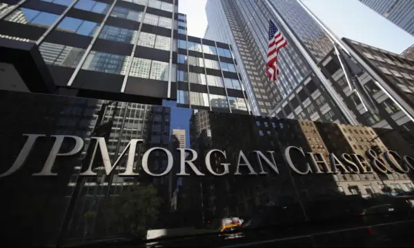 Błyszczący napis JP Morgan Chase & Co na tle drapaczy chmur i amerykańskiej flagi.